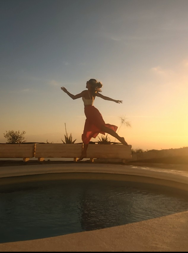 Eine Frau springt mit ausgebreiteten Armen in den Sonnenuntergang
